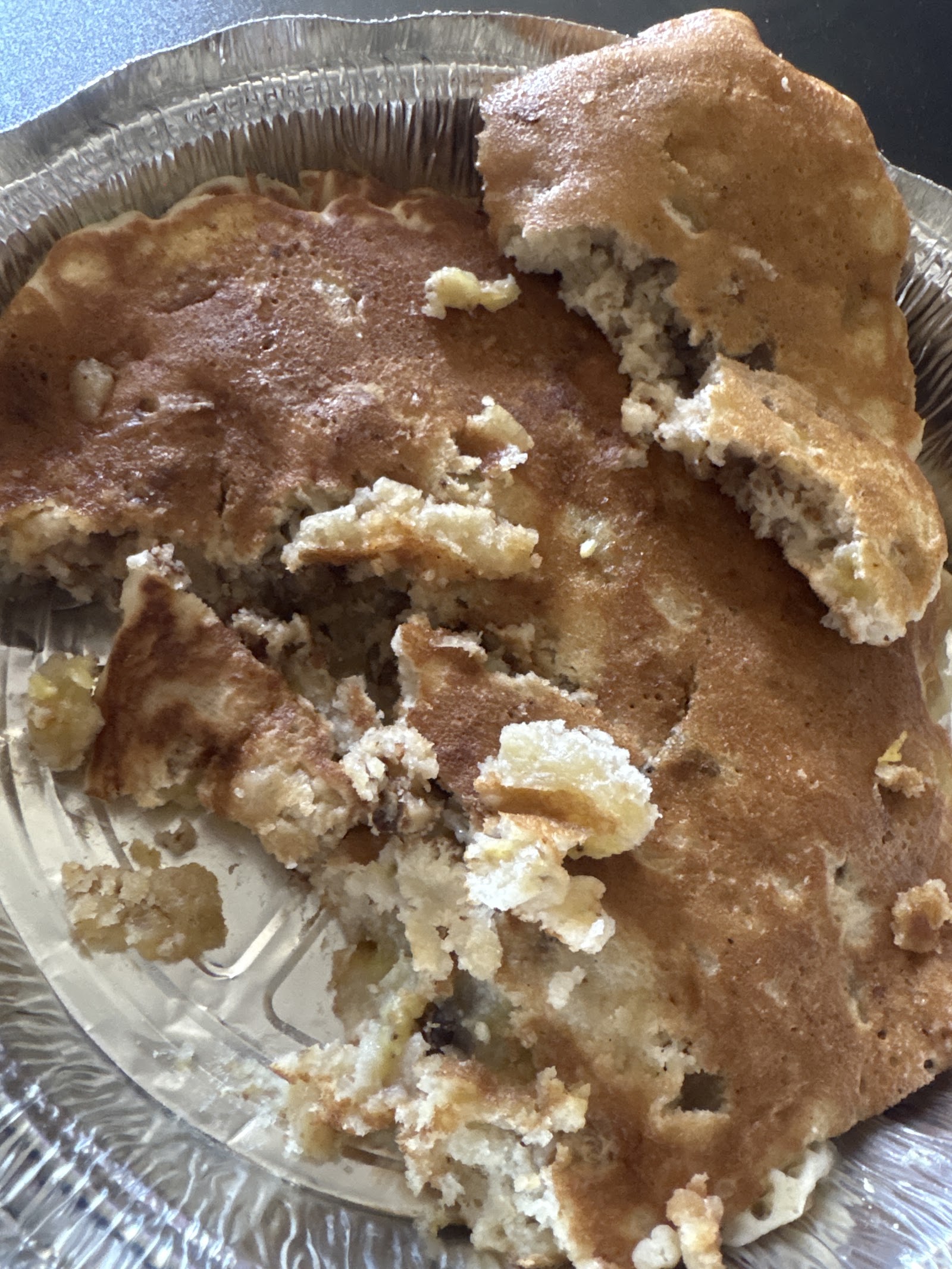 A large pancake broken into pieces in a foil takeout container, golden on top and studded through the crumb